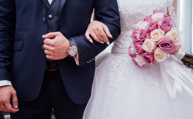 ロングドレスの母親とダークスーツの父親が、新郎新婦のそばで記念撮影をしている光景。